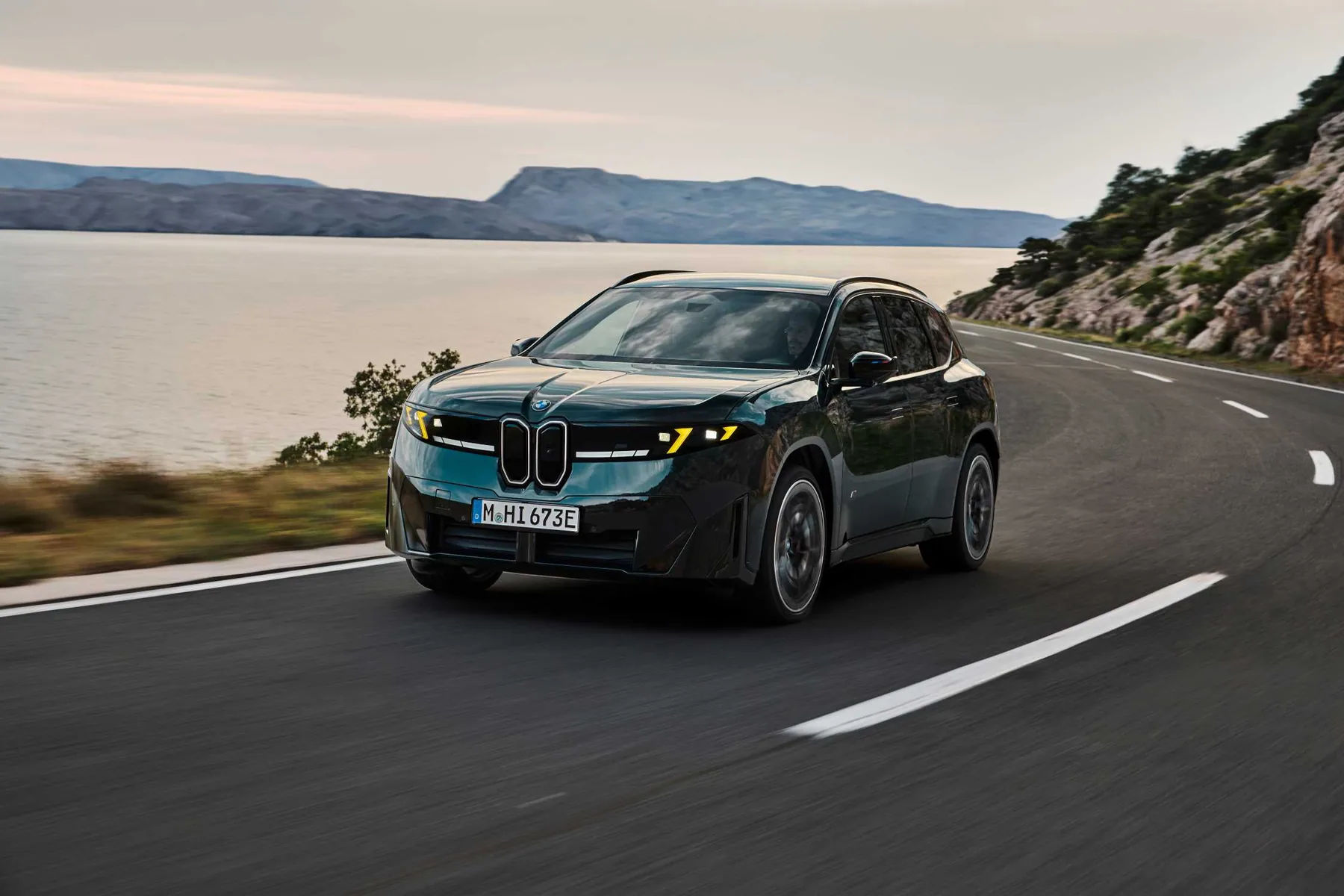 深綠色BMW iX3 M60 xDrive於蜿蜒海岸山路行駛
