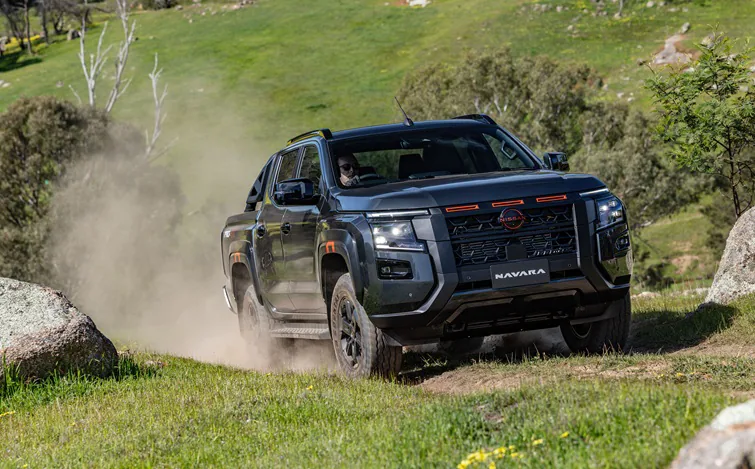 深色Nissan Navara PRO-4X皮卡在林間土路上駛過揚起沙塵