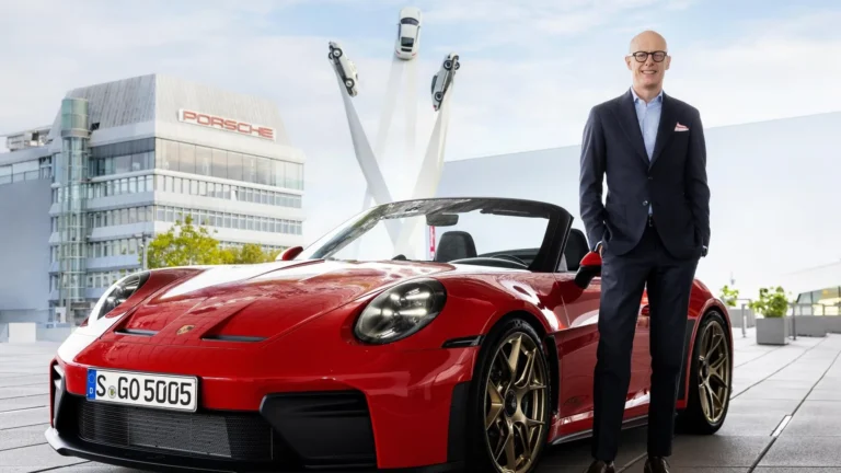Porsche執行長Michael Leiters站在紅色Porsche 911旁，背景為Porsche總部建築，官方2026年照片