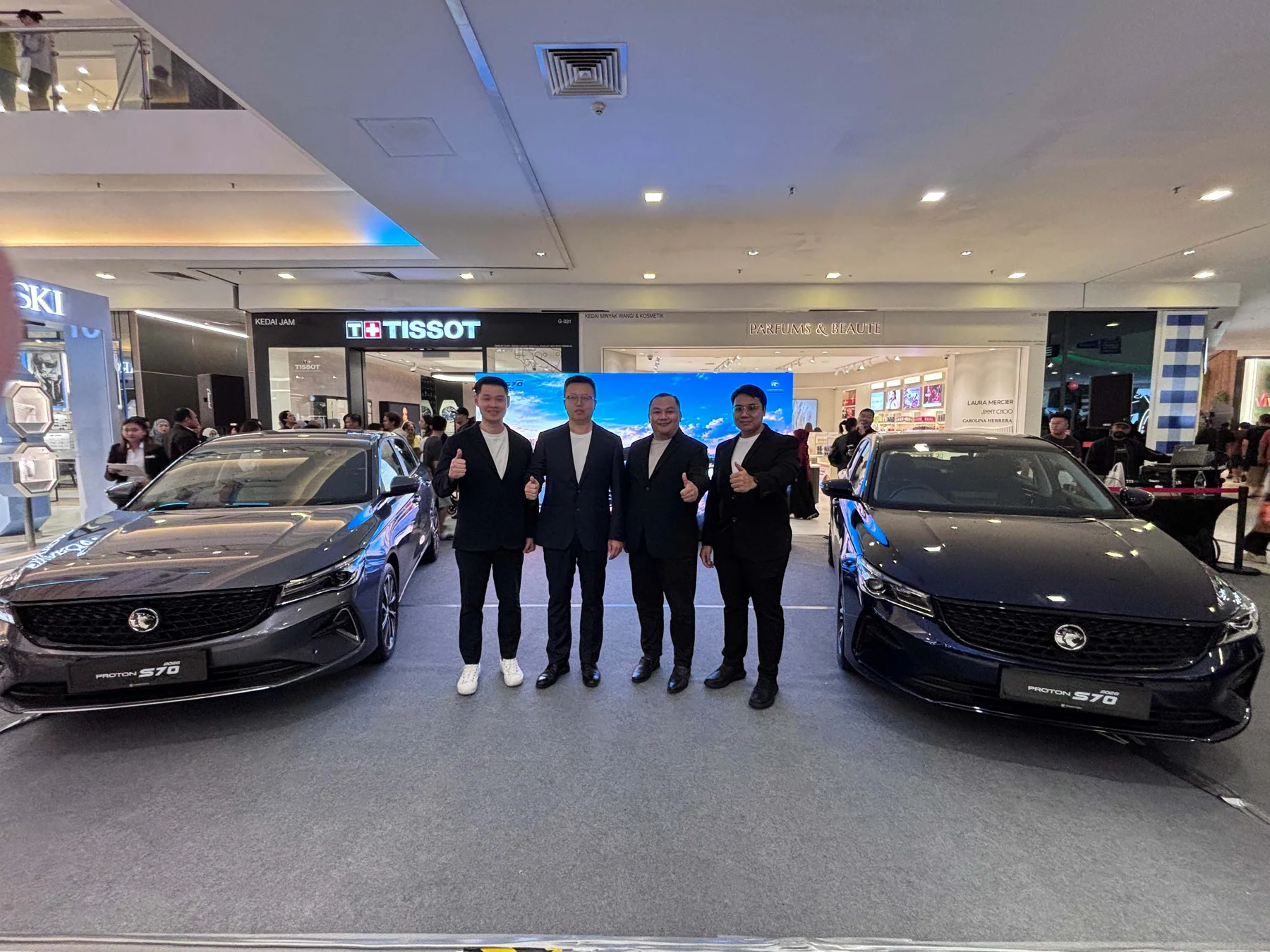 四名嘉賓站在古晉Proton S70路演的兩輛展車之間合影